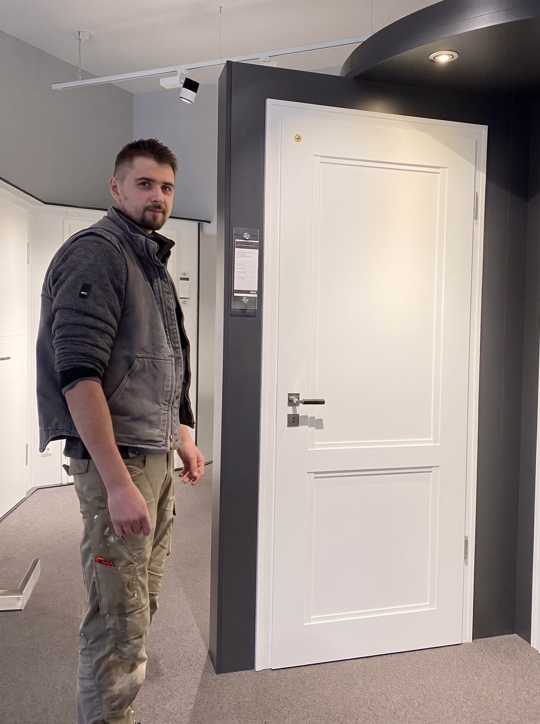 Home 6 Sergej Mai neben einer weißen Innentür in der Ausstellung.