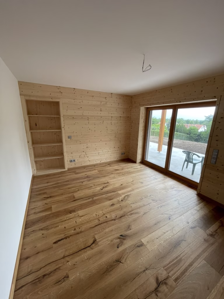 Home 21 Wohnraum mit einem Bodenbelag in markanter Holzoptik, Holz-Wandverkleidung und großer Terrassentür