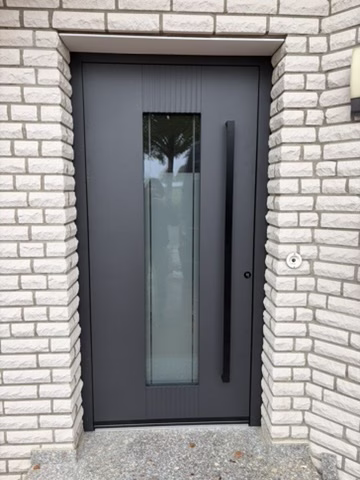 Home 20 Anthrazitfarbene Haustür mit langem senkrechtem Glasausschnitt und schwarzem Griff an einer hellen Klinkerfassade