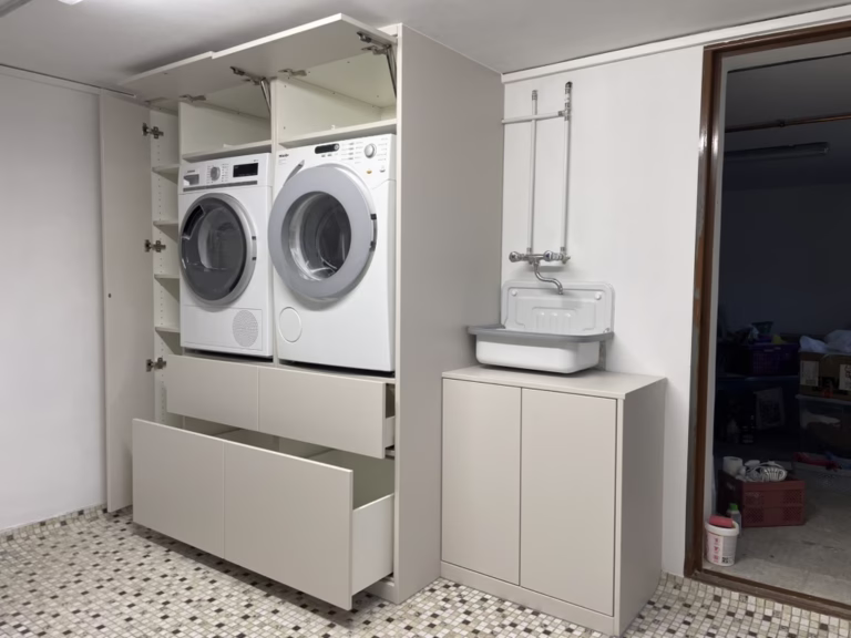 Home 28 Maßgefertigte weiße Schranklösung mit erhöht aufgestellter Waschmaschine und Trockner sowie großen Auszügen