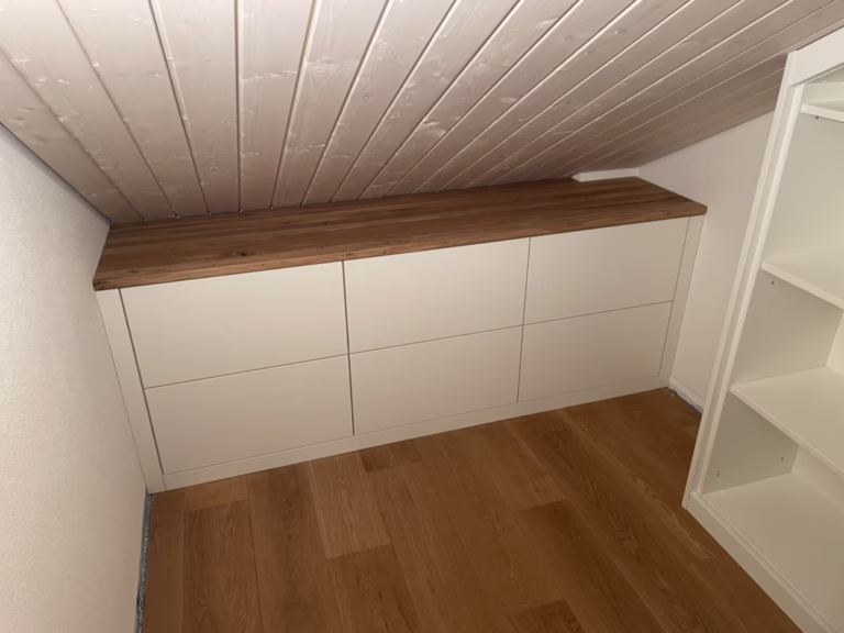 Home 26 Weißes Schubladenmöbel mit Holzplatte passgenau unter einer Dachschräge neben einem Einbauschrank