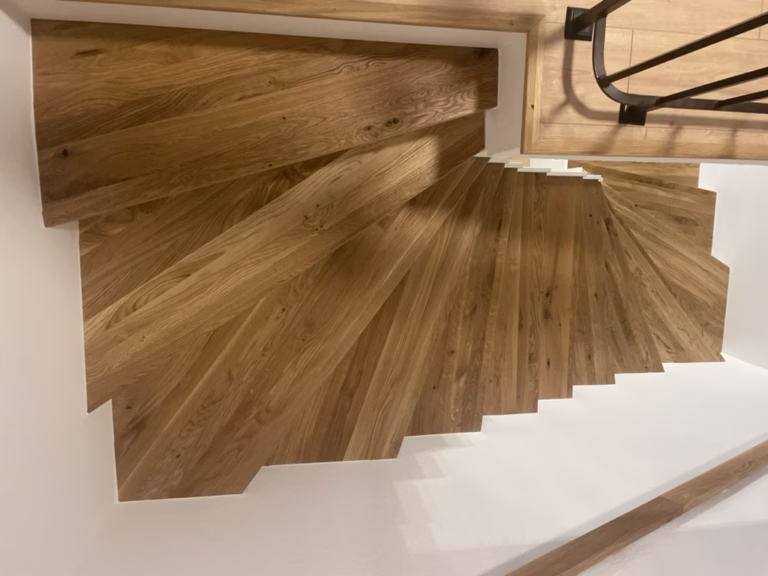 Home 17 Blick von oben auf eine gewendelte Treppe mit Holzstufen und weißen seitlichen Anschlüssen