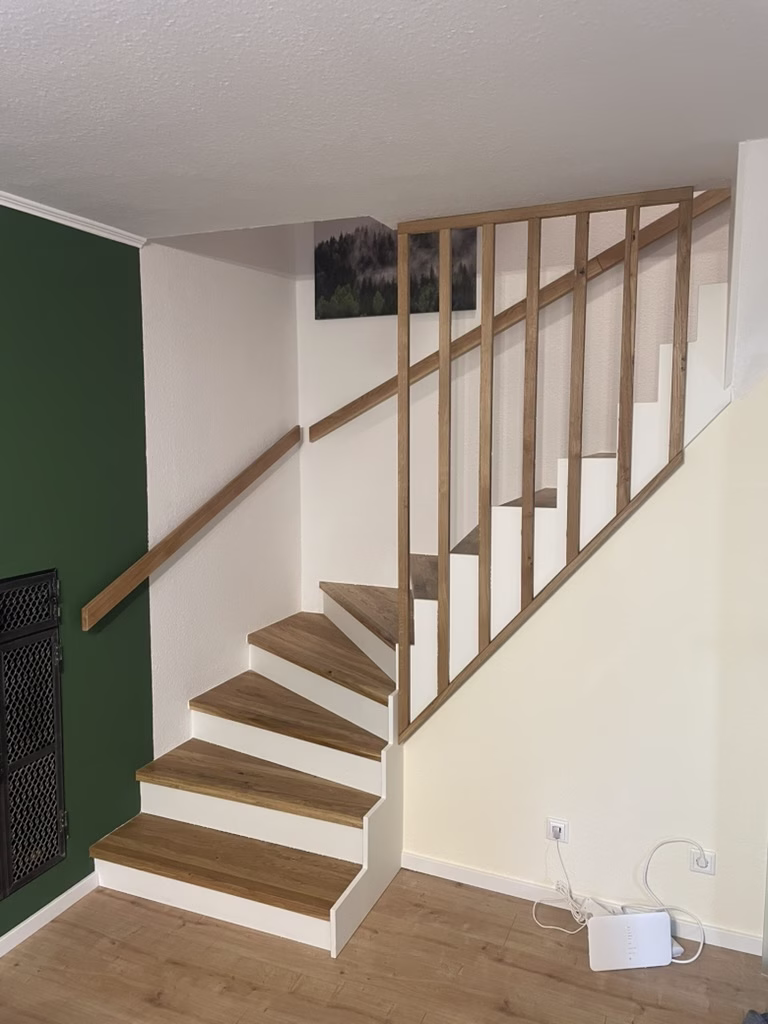 Home 16 Treppe mit Holzstufen, weißen Setzstufen, Holzhandlauf und einem Geländer mit senkrechten Holzstäben