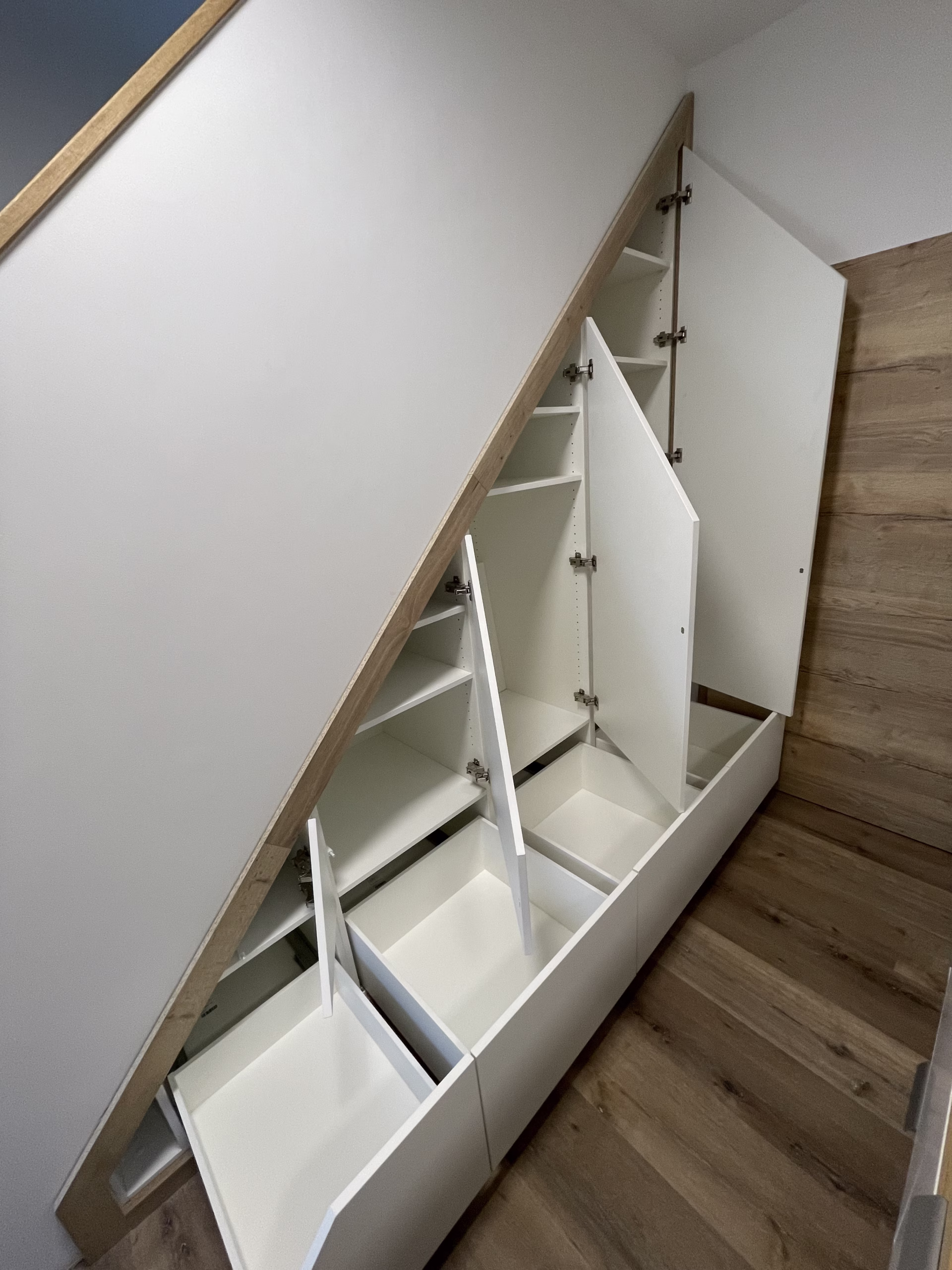 Geöffneter Schrank unter einer Treppe mit Türen und Schubladenauszügen