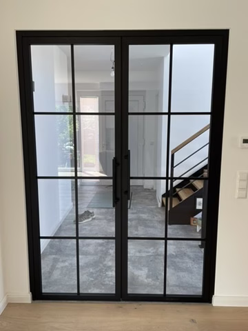 Home 8 Zweiflügeliges schwarzes Lofttürelement mit klarer Verglasung und Sprossen vor einer Treppe