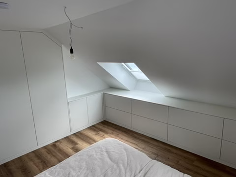 Home 19 Geschlossene weiße Einbauschränke und Schubladenmöbel entlang einer Dachschräge mit Dachfenster