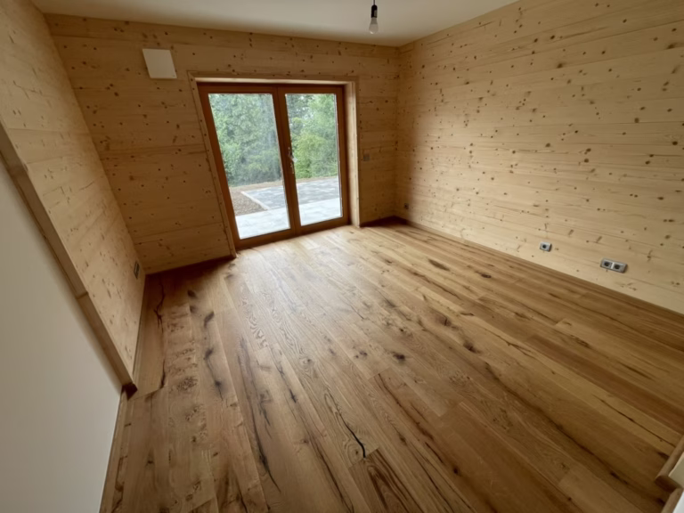 Home 14 Wohnraum mit lebhaft gemasertem Holzboden, Holz-Wandverkleidung und zweiflügeliger Terrassentür